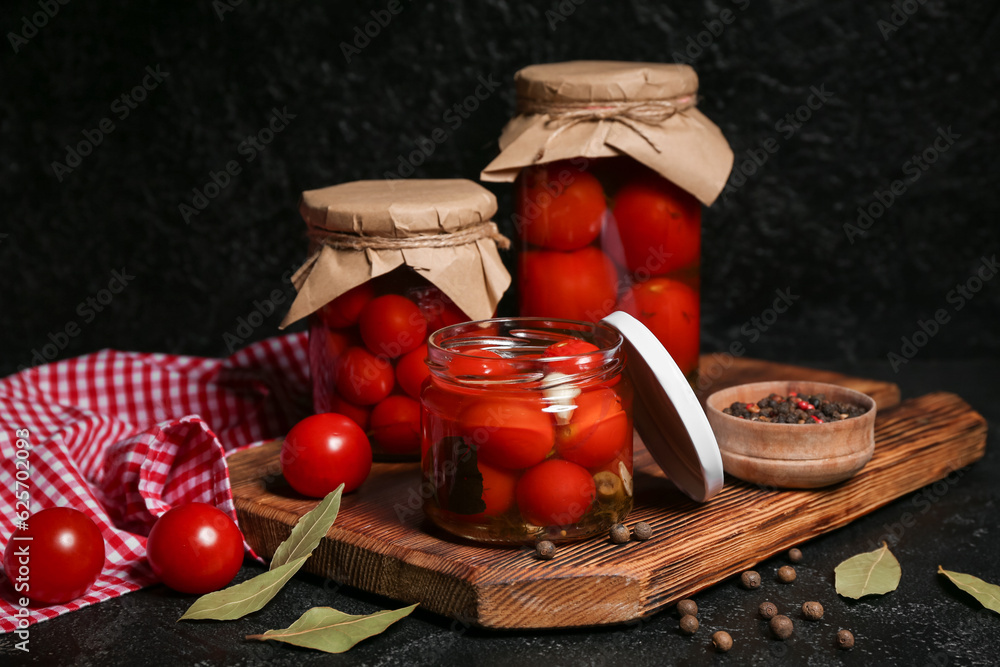 Jars with canned tomatoes and peppercorn on black background