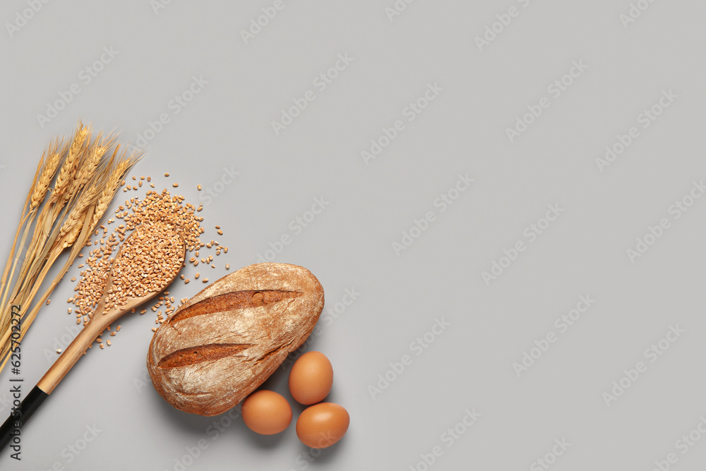 Loaf of fresh rye bread, eggs and wheat grains on grey background