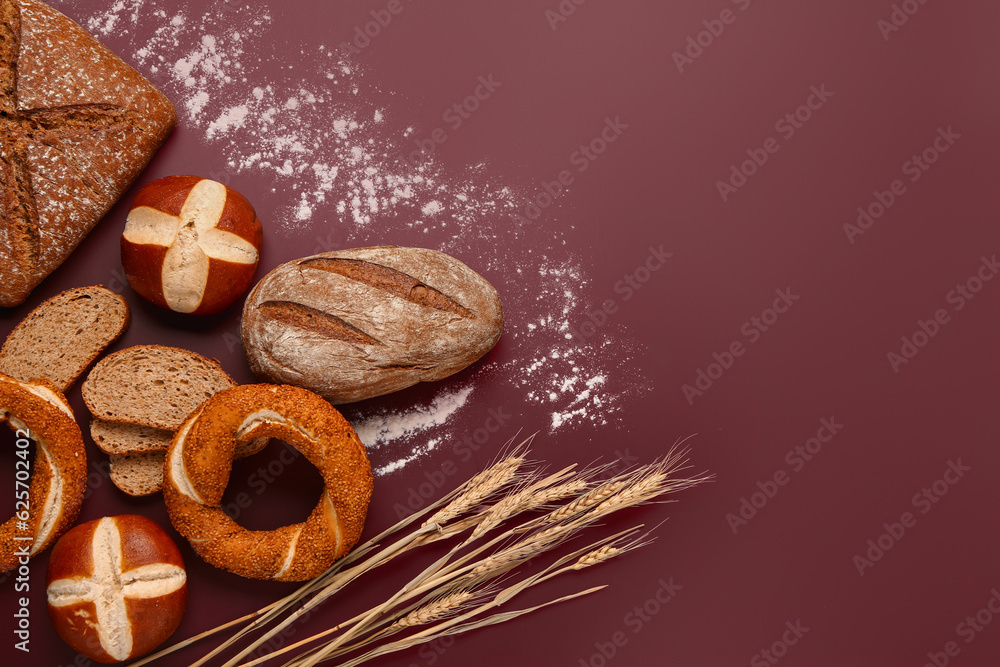 Different types of bread and wheat ears on brown background