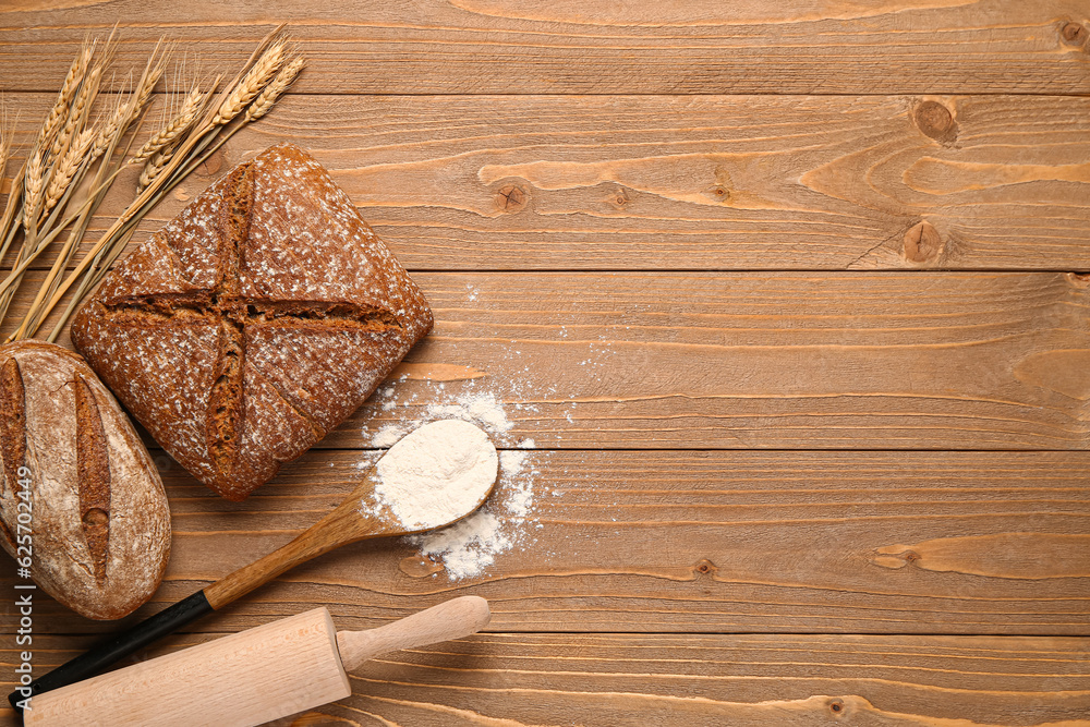 Loaves of fresh rye bread and wheat flour on wooden table