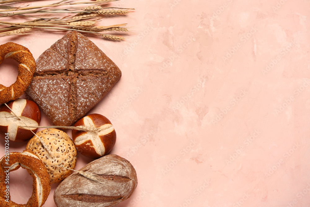 Different types of bread and wheat ears on pink table