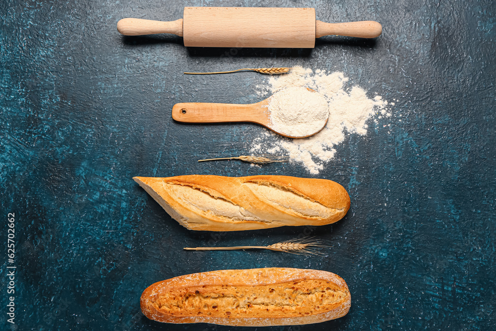 Composition with baguettes, flour, rolling pin and wheat ears on dark blue table