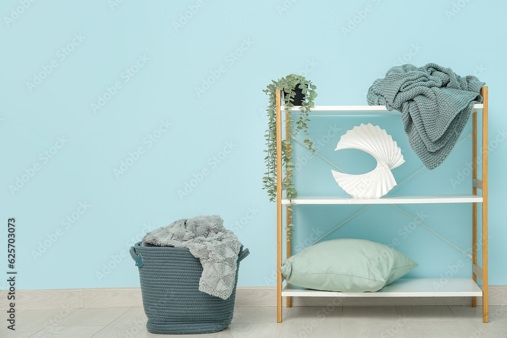 Basket and shelving unit with cozy blankets near blue wall