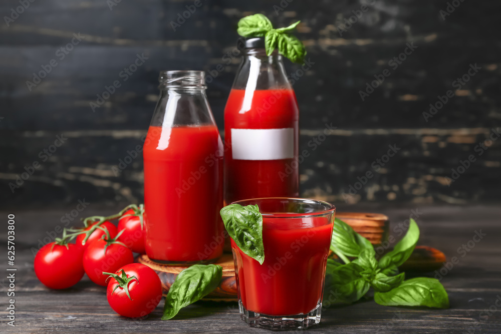 Bottles and glass of tasty juice on black wooden background