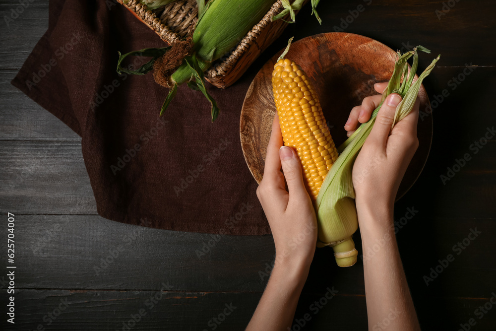 Woman peeling corn cob on black wooden table