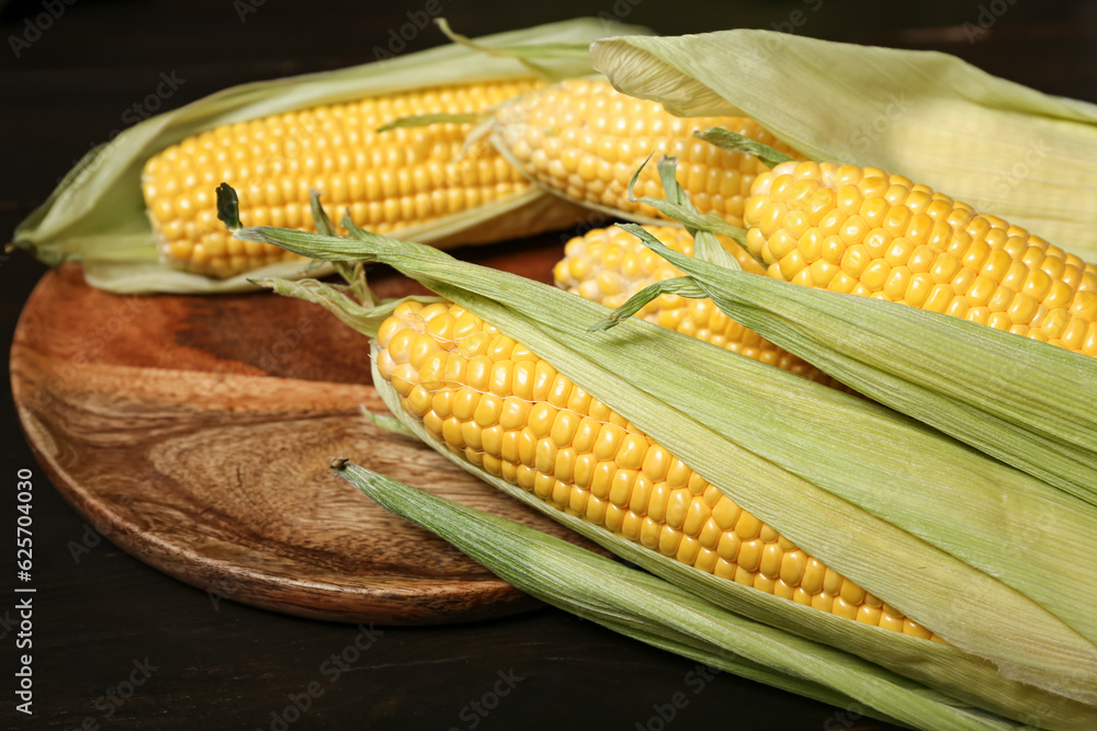 Plate with fresh corn cobs on black wooden table