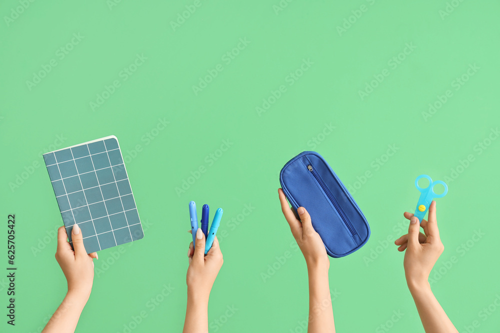 Female hands with school accessories on green background