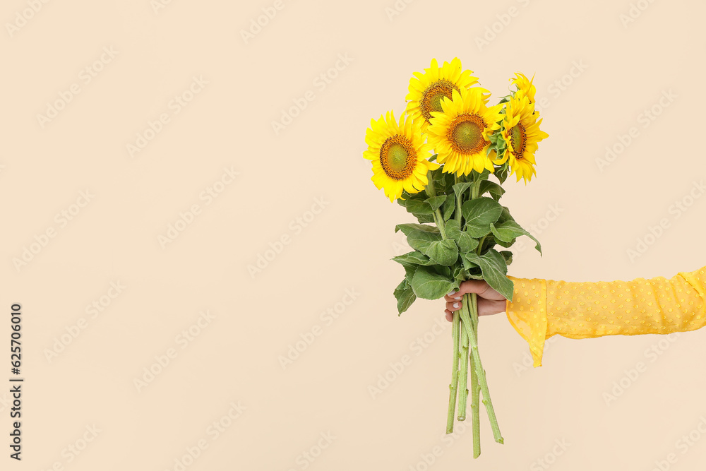 Young woman with beautiful sunflowers on beige background