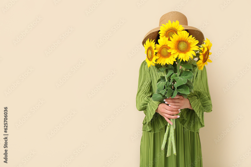 Young woman with beautiful sunflowers on beige background