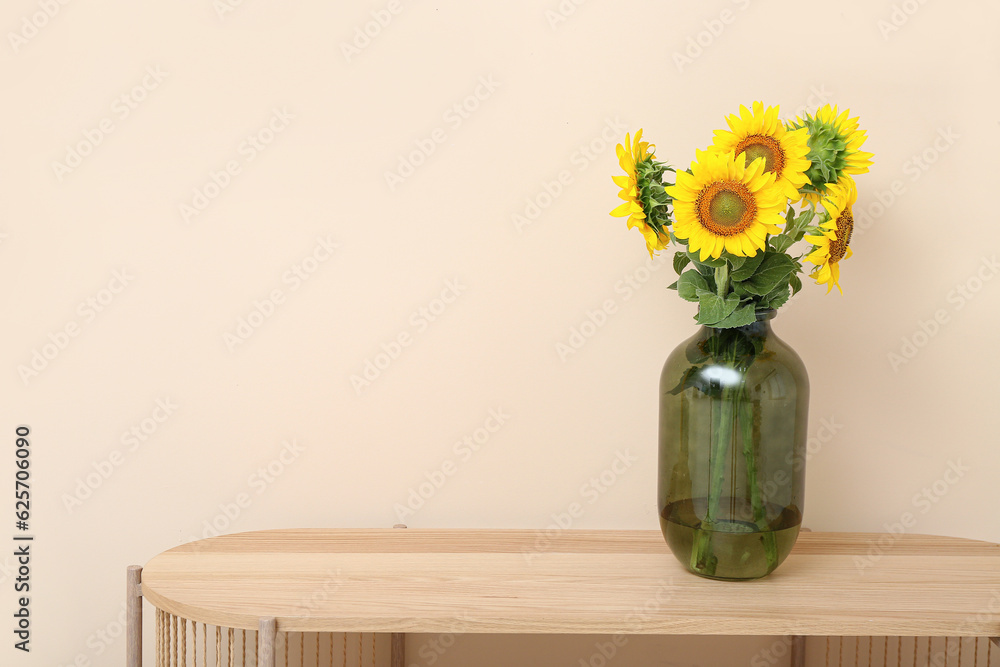 Vase with sunflowers on table near beige wall