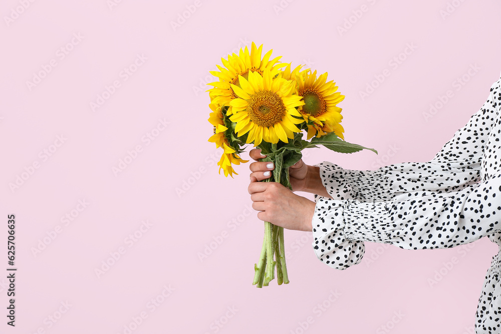 Young woman with beautiful sunflowers on pink background