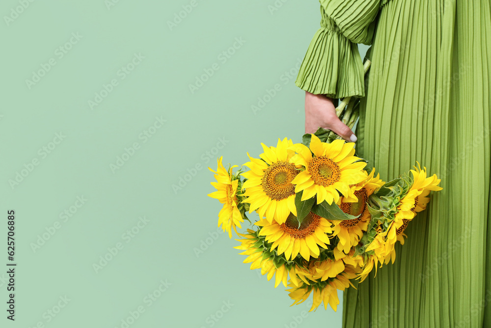 Young woman with beautiful sunflowers on green background, closeup