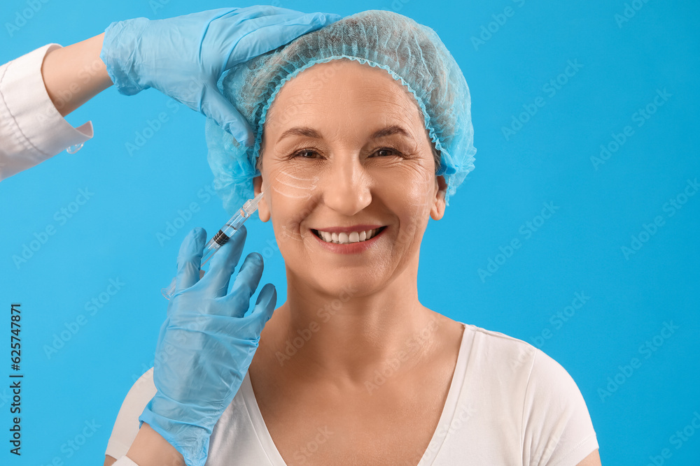 Mature woman receiving filler injection on blue background, closeup