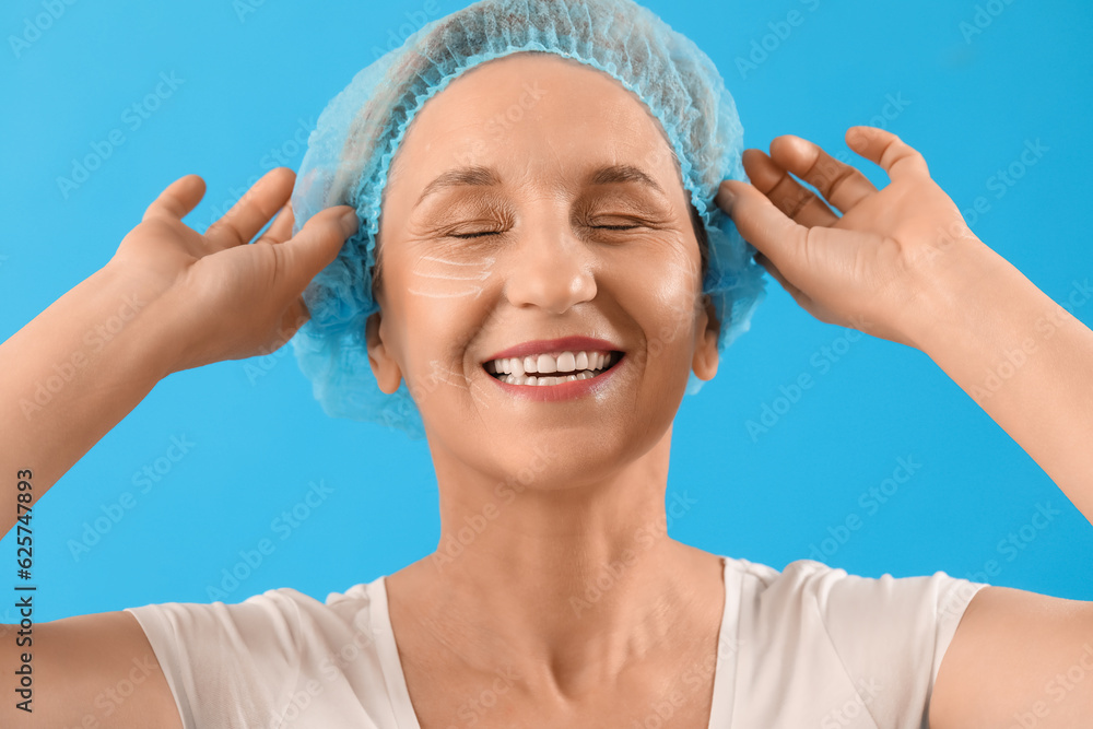 Happy mature woman with marked face for filler injection on blue background, closeup