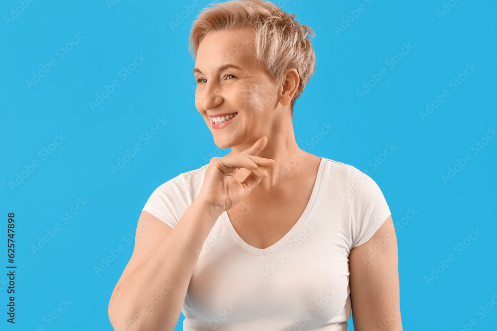 Mature woman with marked face for filler injection on blue background, closeup