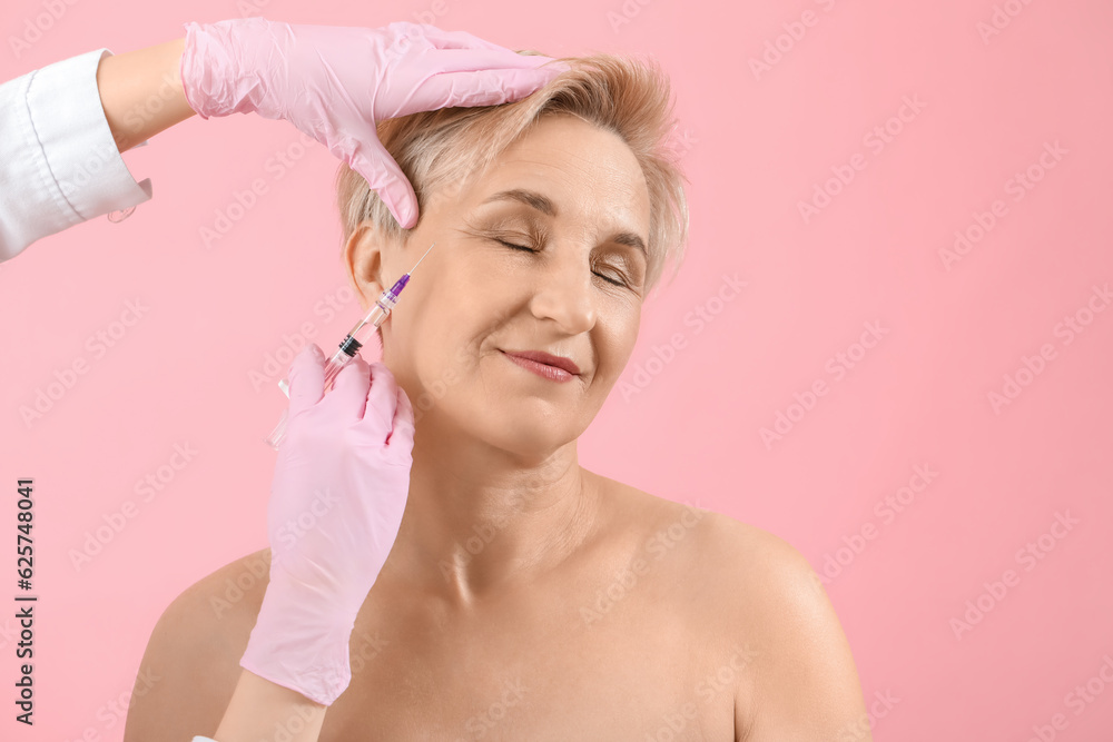 Mature woman receiving filler injection on pink background, closeup