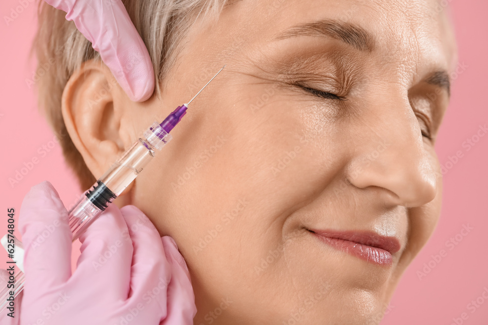 Mature woman receiving filler injection on pink background, closeup