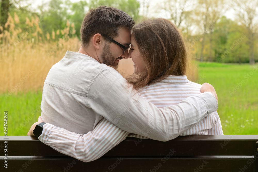 Beautiful loving couple sitting on bench and hugging in park