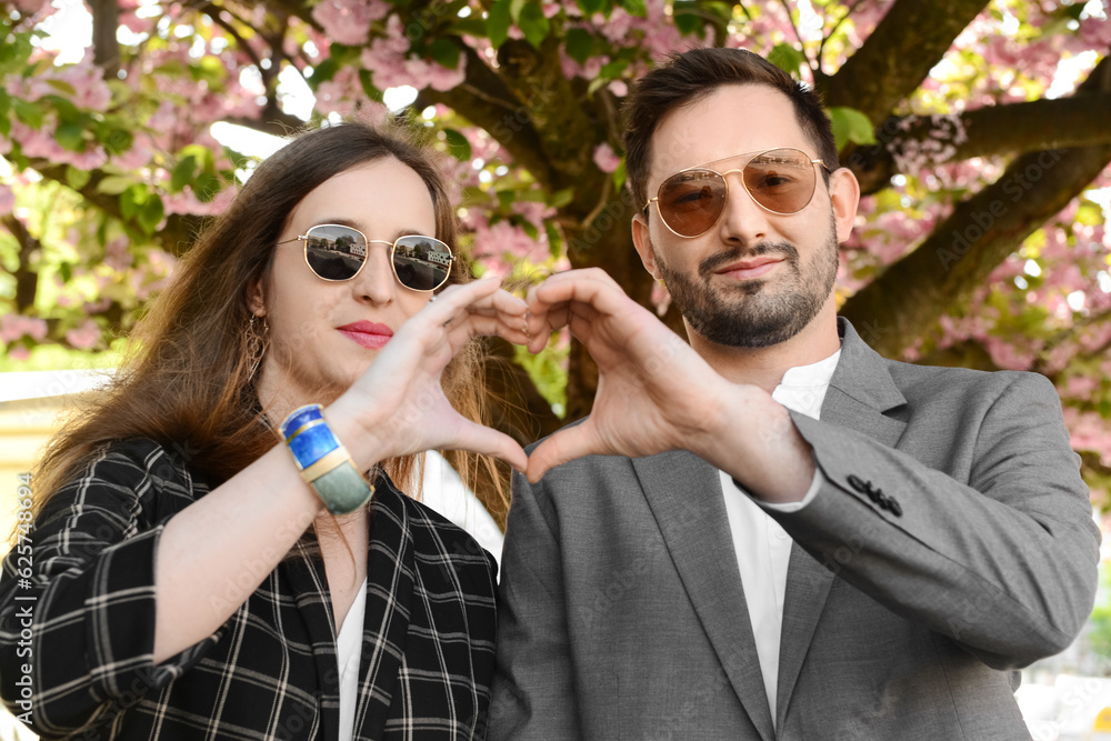 Beautiful happy couple making heart shape with their hands near blooming tree on sunny spring day