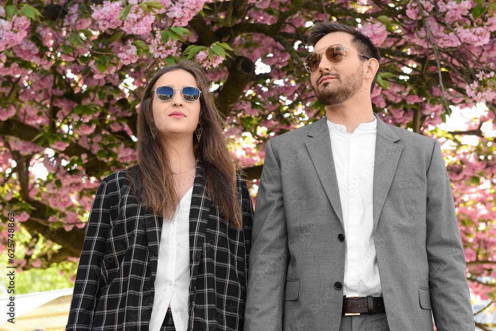 Beautiful loving young couple holding hands near blooming tree on sunny spring day