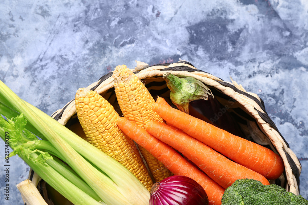 Wicker bowl with different fresh vegetables on blue background, closeup