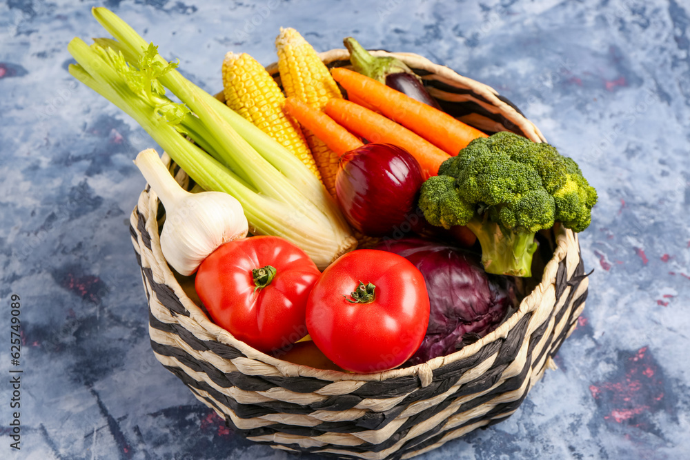 Wicker bowl with different fresh vegetables on blue background