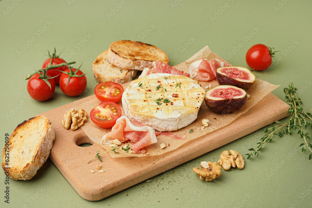 Wooden board with tasty baked Camembert cheese on green background