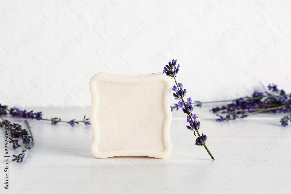 Soap bar and lavender flowers on light wooden table