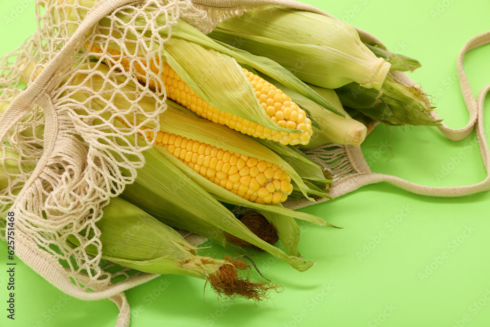 String bag with fresh corn cobs on green background