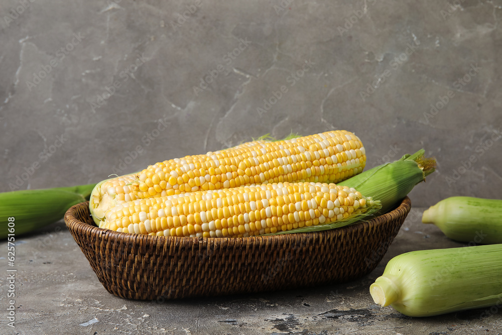 Wicker bowl with fresh corn cobs on grey background