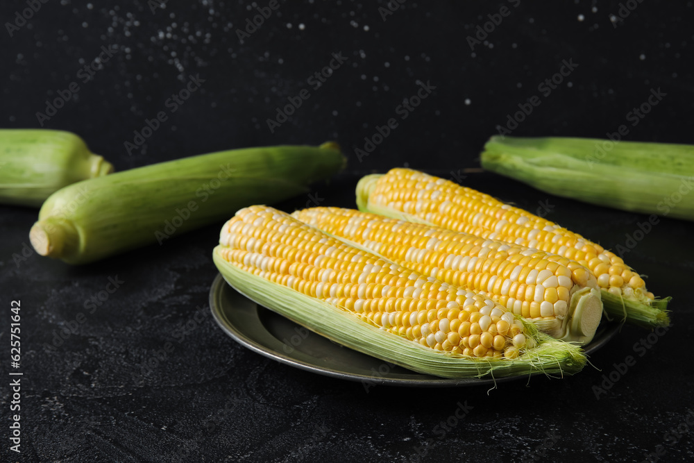 Plate with fresh corn cobs on black background