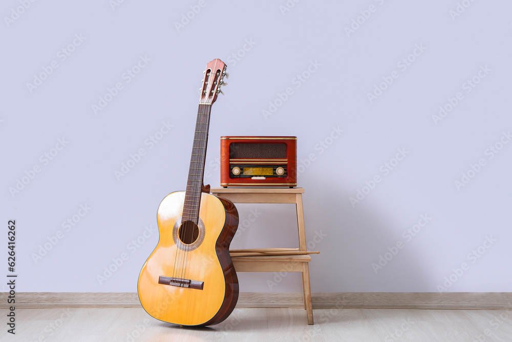 Retro radio receiver and guitar near light wall