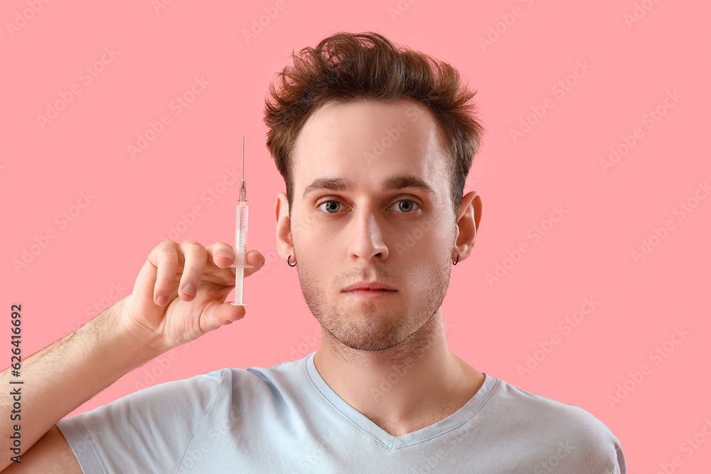 Young man with injection for hair growth on pink background, closeup