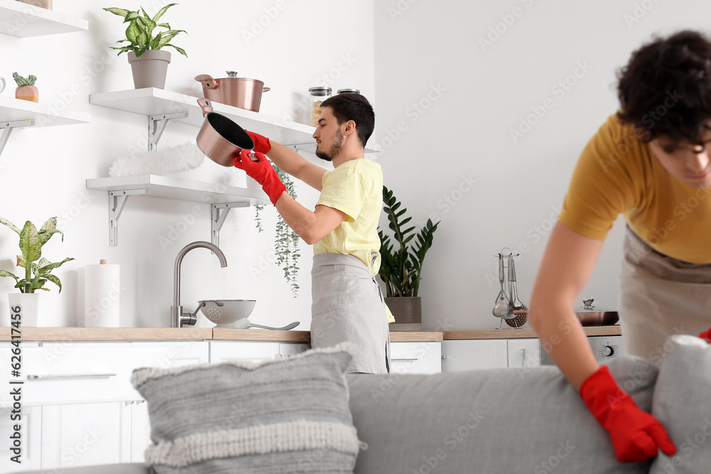 Male janitor cleaning shelf with pp-duster in kitchen