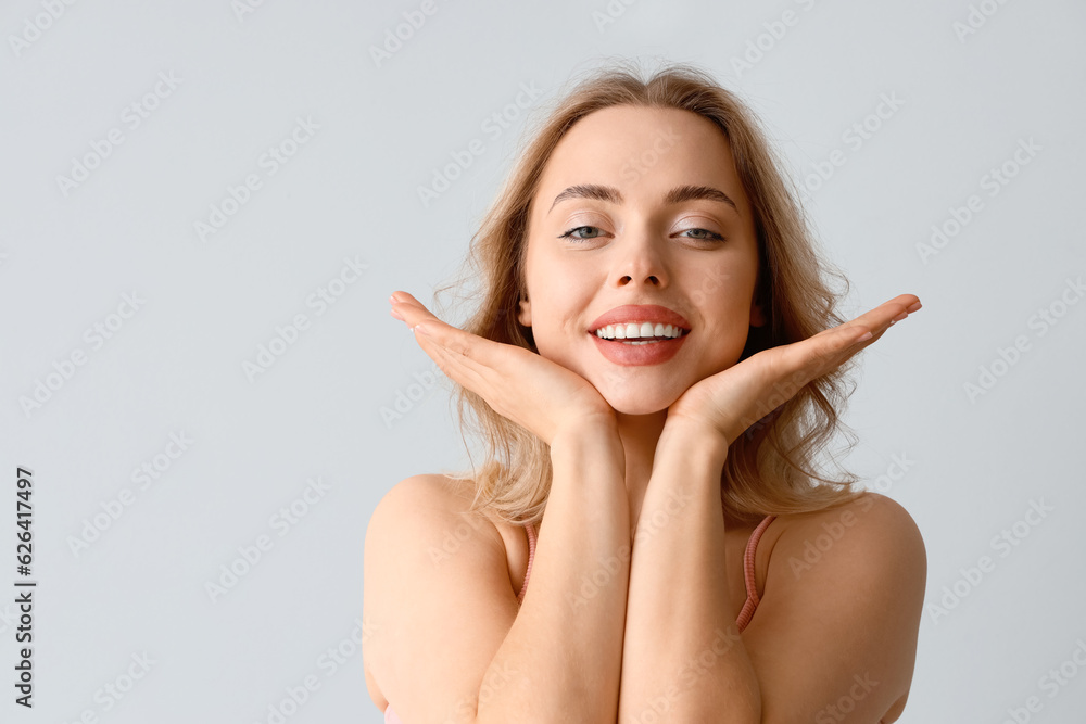 Young woman doing face building exercise on light background