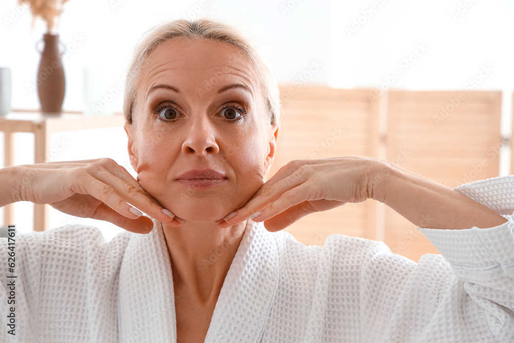 Mature woman doing face building exercise in bathroom, closeup