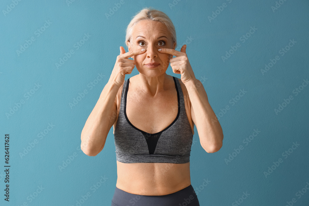 Sporty mature woman doing face building exercise on blue background