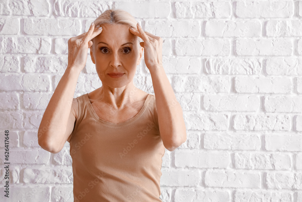 Mature woman doing face building exercise on white brick background