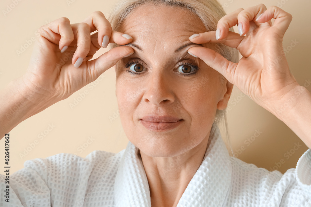 Mature woman doing face building exercise on beige background, closeup