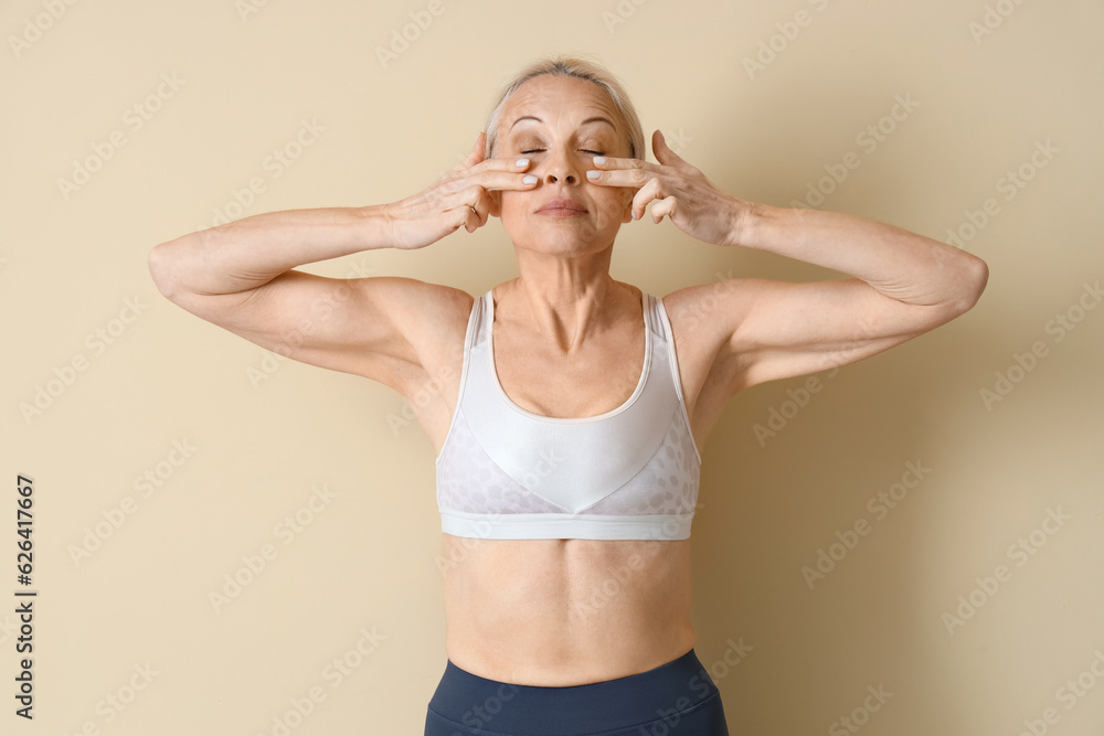 Sporty mature woman doing face building exercise on beige background