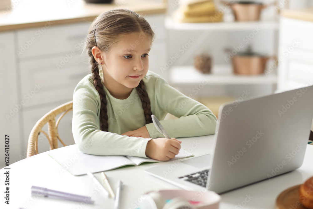 Little girl with laptop studying computer sciences online in kitchen