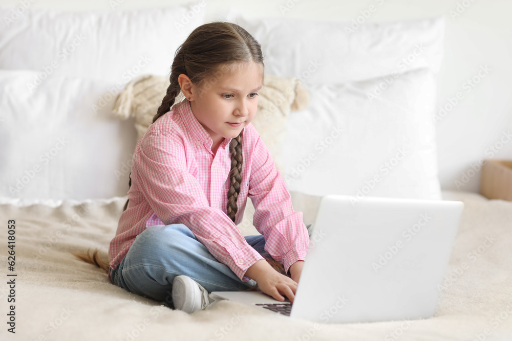 Little girl with laptop studying computer sciences online in bedroom