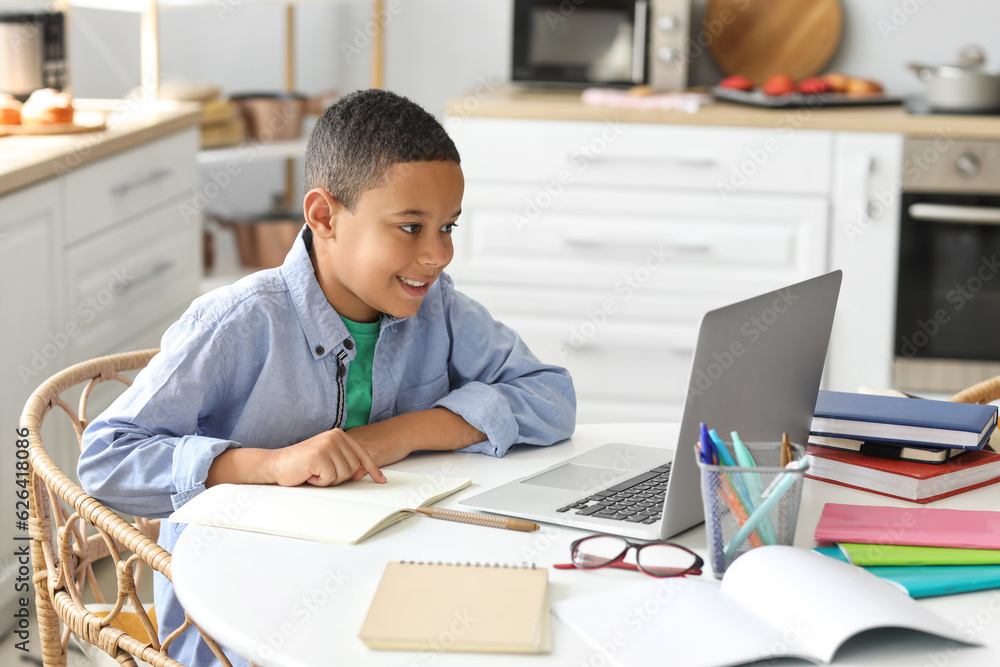 Little African-American boy studying computer sciences online in kitchen