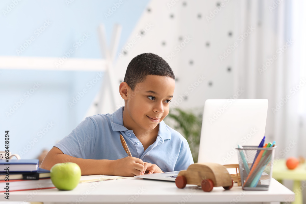 Little African-American boy studying computer sciences online in bedroom