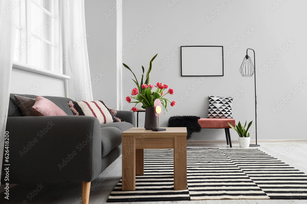 Interior of light living room with sofa, bench, coffee table and tulip flowers