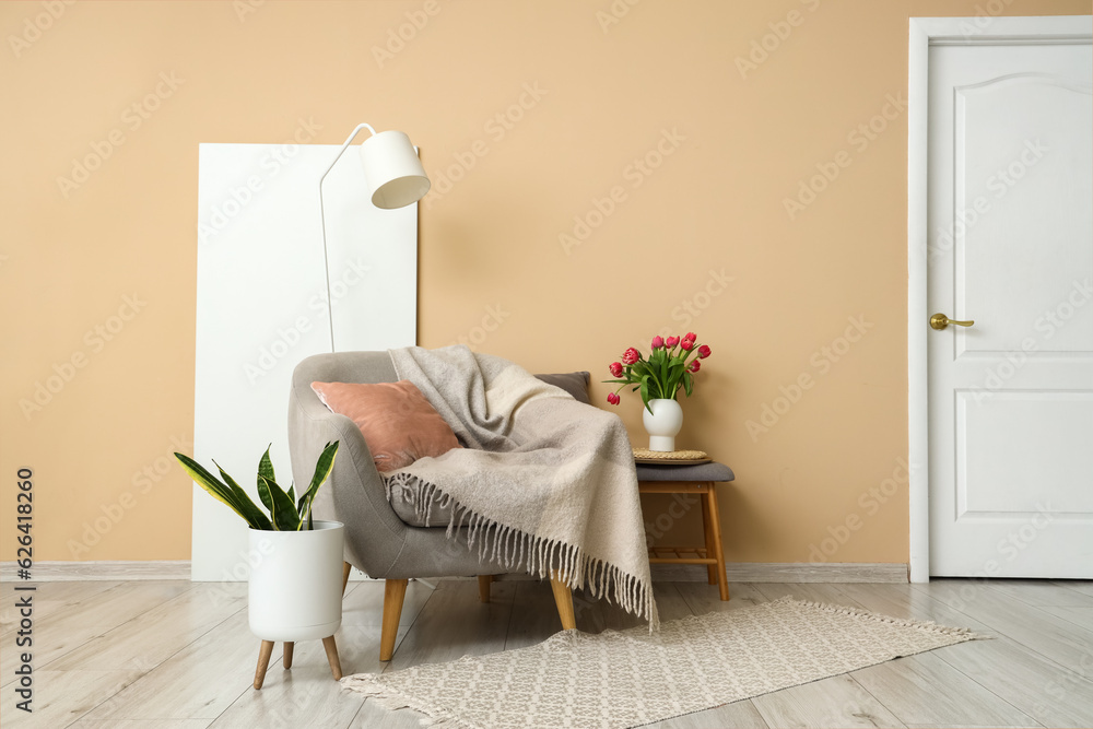 Grey armchair and vase with tulip flowers on grey armchair near beige wall