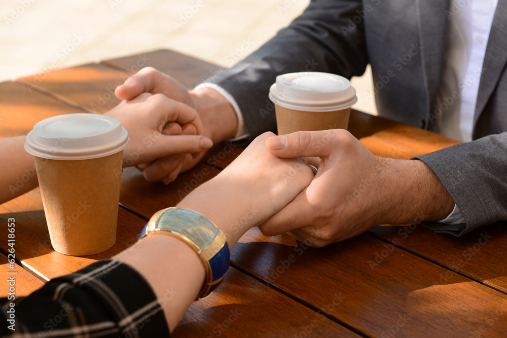 Beautiful couple sitting in cafe, drinking coffee and holding hands on sunny spring day