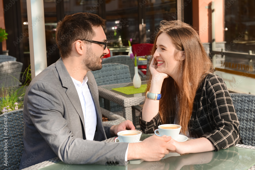 Beautiful happy loving couple sitting in restaurant and drinking coffee on sunny spring day