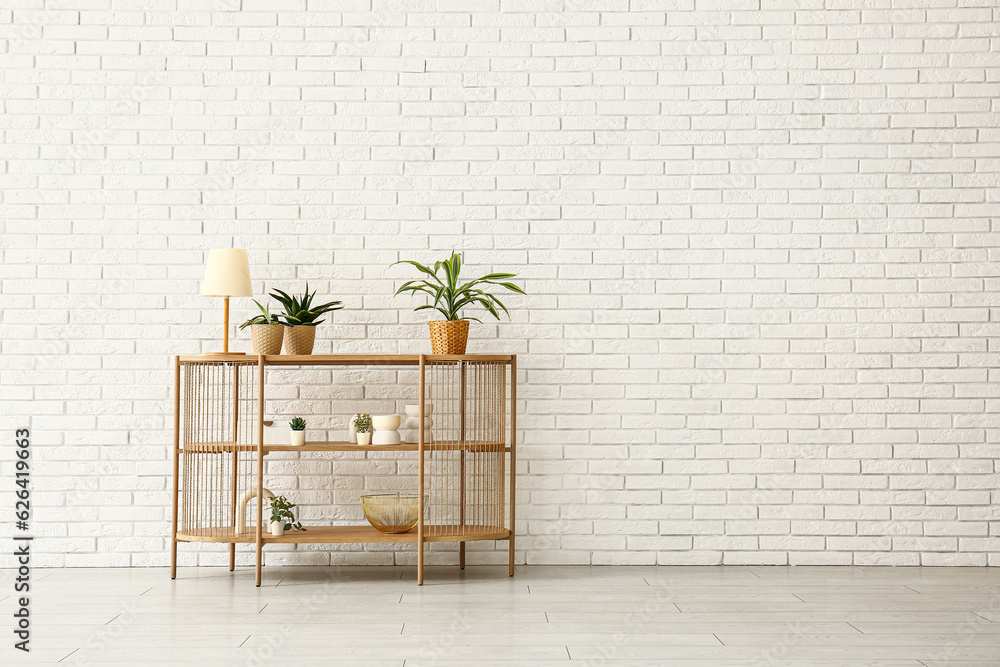 Table with houseplants and lamp near white brick wall in room