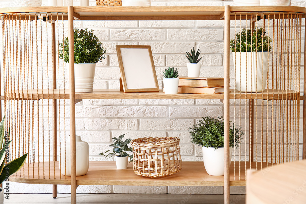 Table with houseplants, frame and books near white brick wall